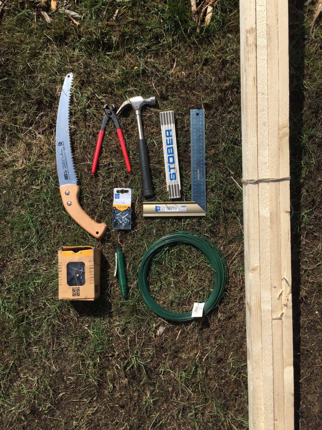 Material und Werkzeug, das man für das Errichten einer Rankhilfe aus Holz und Draht benötigt, liegt auf einem Rasen.