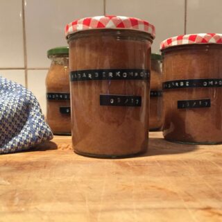 Auf einem Holzbrett stehen mehrere Gläser mit Rhabarberkompott, die mithilfe eines Dymo-Gerätes beschriftet wurden.