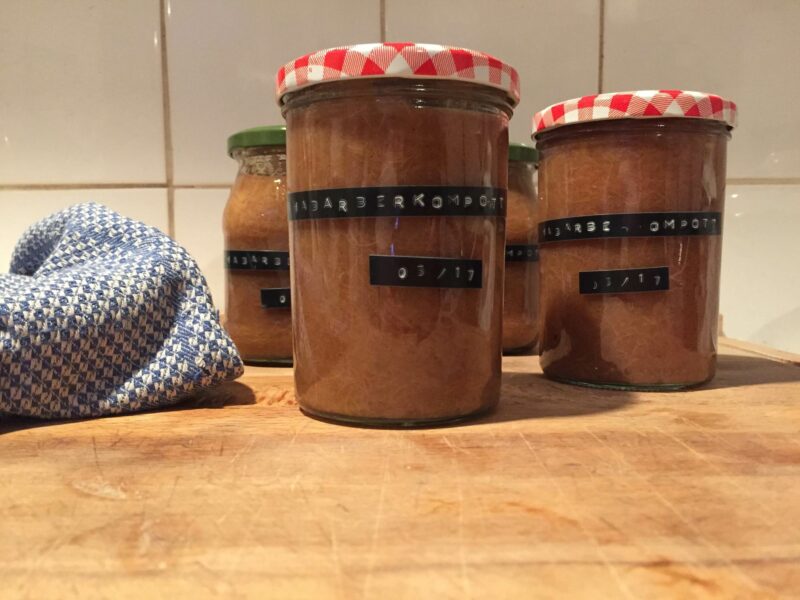 Auf einem Holzbrett stehen mehrere Gläser mit Rhabarberkompott, die mithilfe eines Dymo-Gerätes beschriftet wurden.