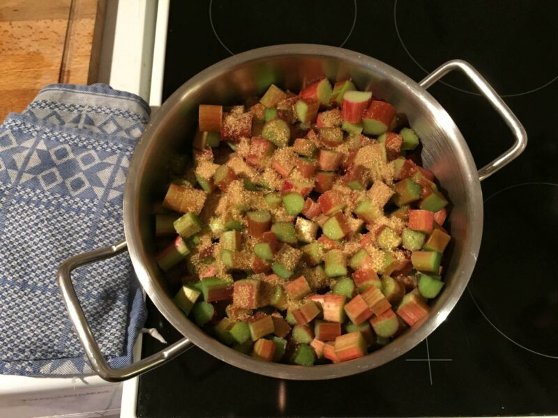 Gezuckerte Rhabarberstückchen liegen in einem Topf auf einem Herd.