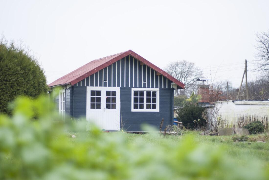 Blick auf eine Anthrazit-farbene Gartenhütte mit rotem Dach und weißen Giebellatten.
