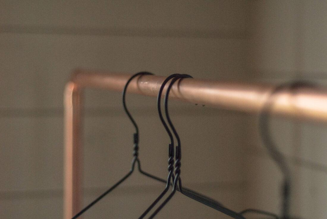Schwarze Kleiderbügel hängen auf einer DIY-Kleiderstange aus Kupferrohr.