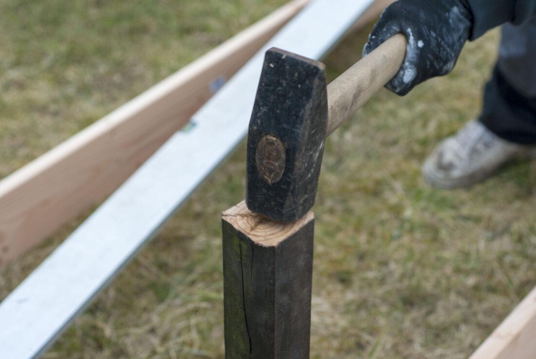 Mit dem Vorschlaghammer und einem Stück Restholz wird eine Einschlaghülsen in den Boden gerammt. 