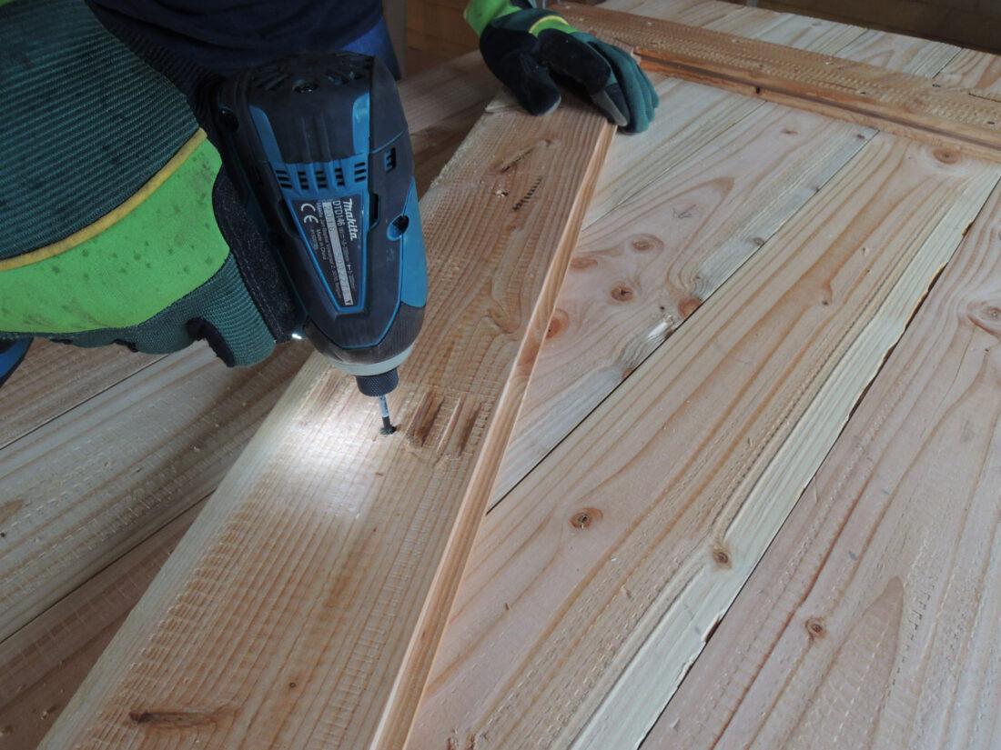 Close-up eines Mannes, der eine Z-Verbindung auf Holzlatten fixiert, um eine Holztür selber zu bauen.