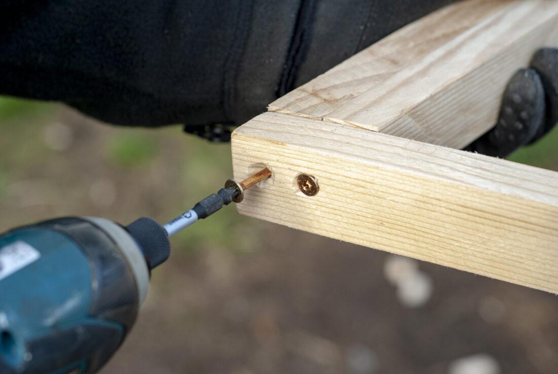  Weihnachtsbaum selber bauen: Close-up eines Akku-Schraubers, mit dem zwei Schrauben in eine Holzkonstruktion getrieben werden. 