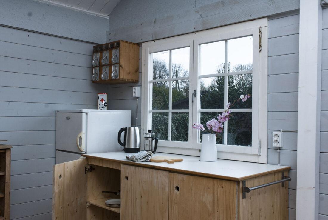 Eine DIY-Küchenzeile steht neben einem Kühlschrank vor dem Fenster einer Gartenhütte. 