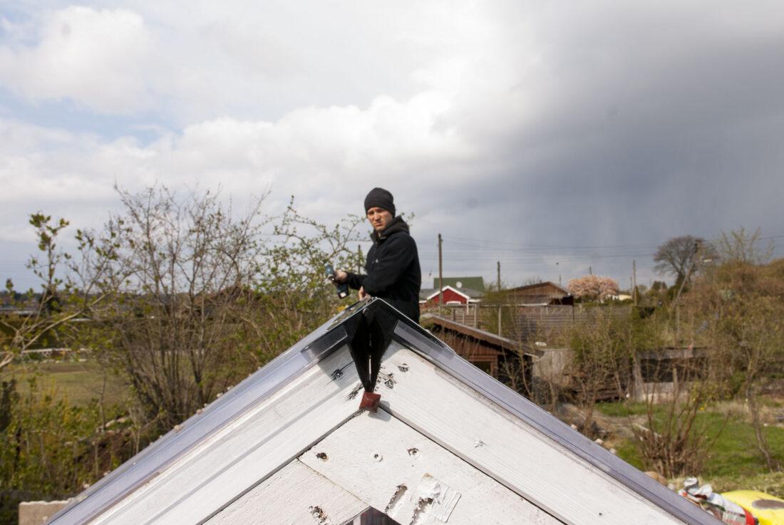 Ein Mann montiert den Dachfirst auf einem selbst gebauten Gewächshaus. 