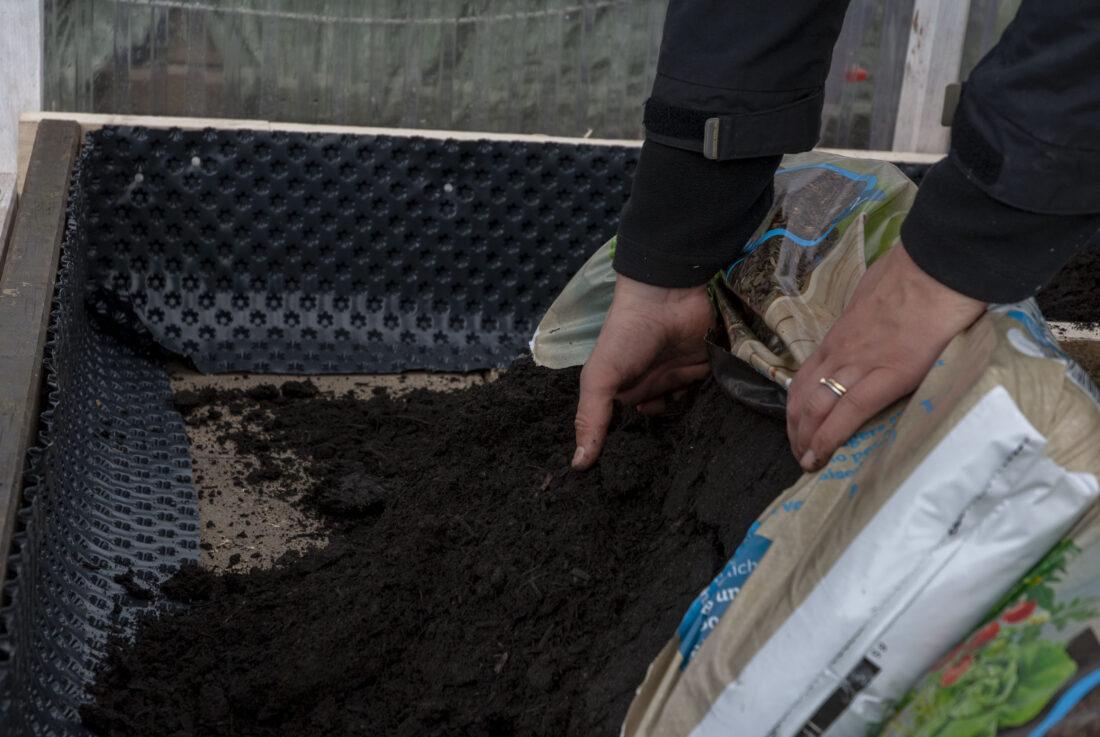 Gewächshaus von innen gestalten: Eine Frau gibt Kompost in ein Beet. 