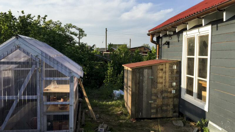Neben einer selbst gebauten Gartenhütte steht ein mit Holz verkleideter IBC-Container.