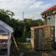 Neben einer selbst gebauten Gartenhütte steht ein mit Holz verkleideter IBC-Container.