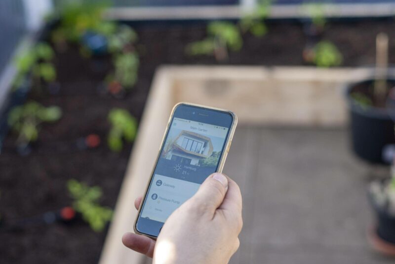 Smart bewässern: Ein Mann steht mit einem Smartphone vor einem Beet.