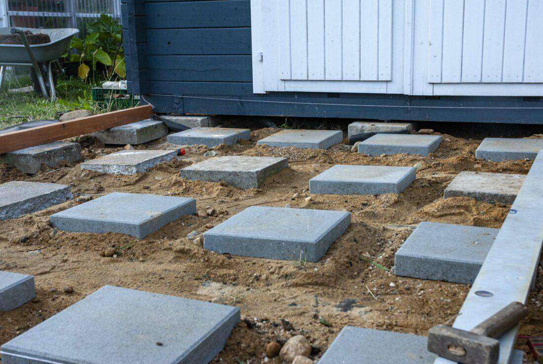Fundamente für eine selbst gebaute Holzterrasse liegen vor einer Gartenhütte. 
