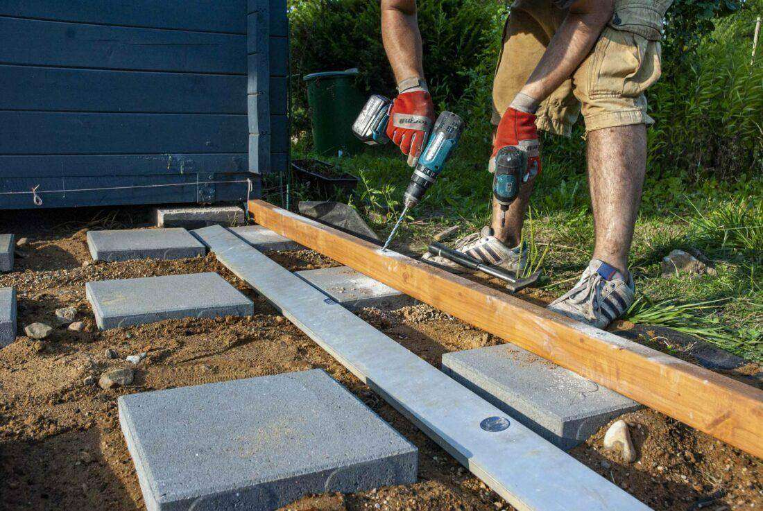 Holzterrasse bauen: Ein Mann verlegt eine Unterkonstruktion.