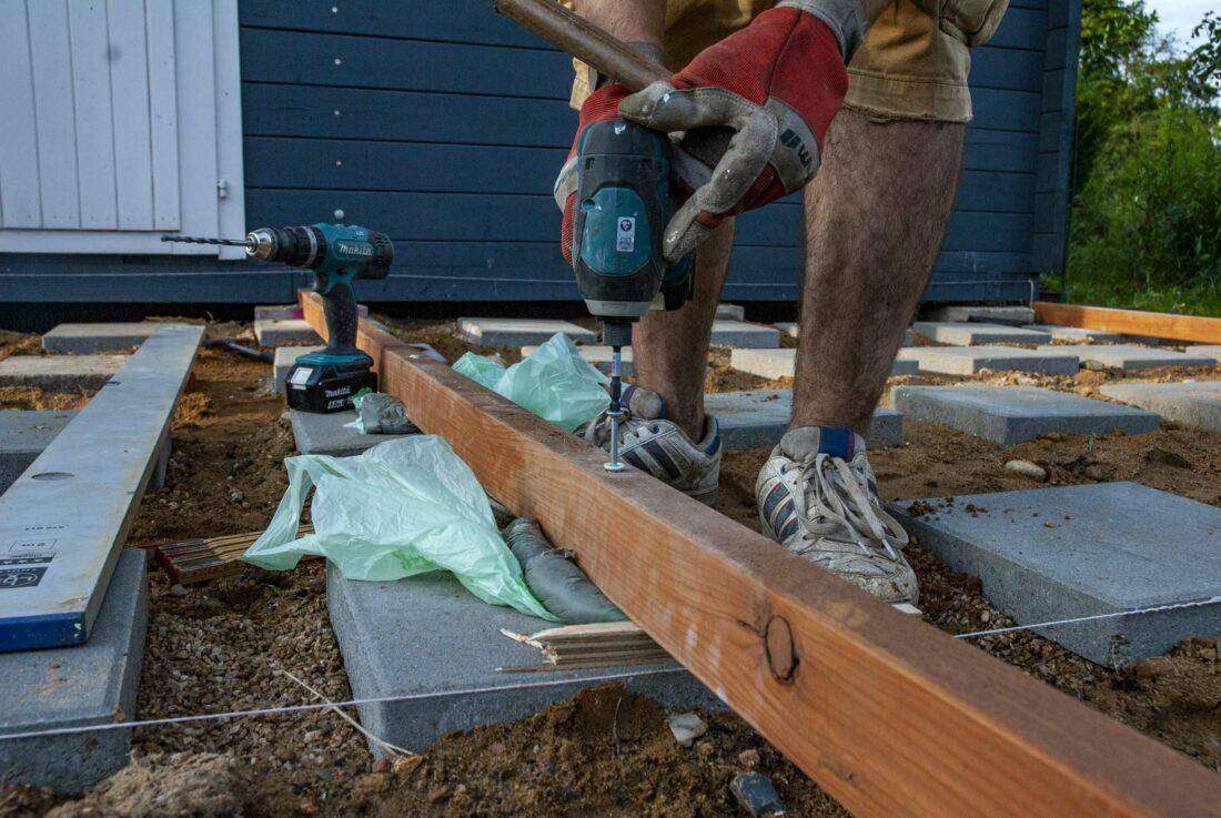 Holzterrasse bauen: Ein Mann verlegt Kanthölzer für die Unterkonstruktion einer Holzterrasse.