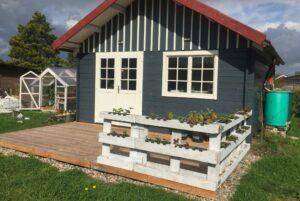 Terrassengeländer aus Paletten: eine Gartenhütte mit einem Geländer, in das Erdbeeren gepflanzt sind.