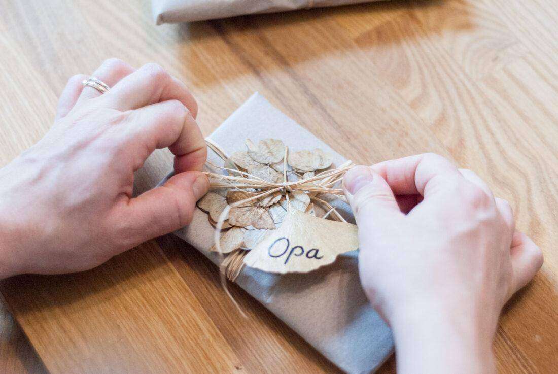 Eine Frau befestigt ein selbst gebasteltes Namensschildchen aus einem Ginkgo-Blatt an einem Geschenk. 