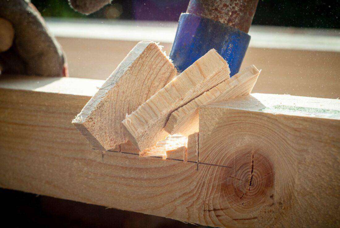Ein Mann stemmt kleine Holzklötze für eine Überblattung aus einem Kantholz. 