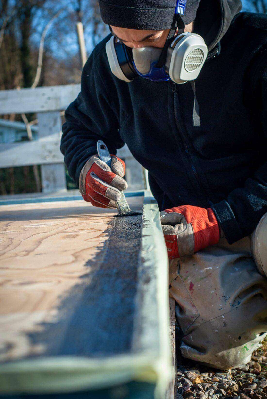 Ein Mann streicht das Dach einer DIY-Außenküche mit Abdichtmasse. 