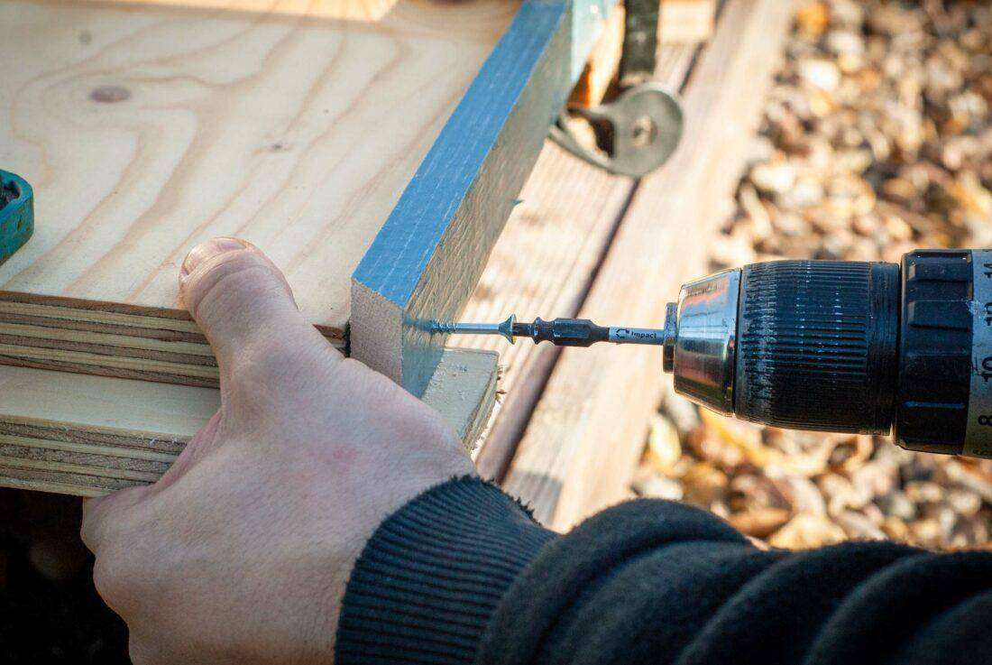 Außenküche selber bauen: Ein Mann schraubt eine Dachlatte an eine Platte.