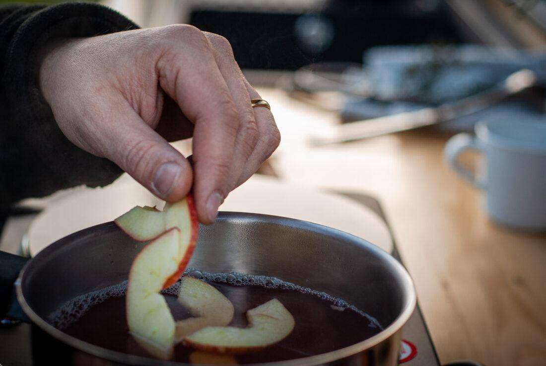 Ein Mann gibt Apfelschnitze in einen Topf mit Quittenpunsch.