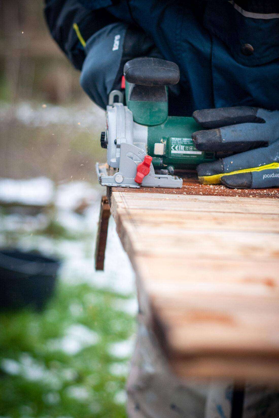 Gartentisch selber bauen: Ein Mann sägt die Kanten von mehreren Holzdielen ab. 