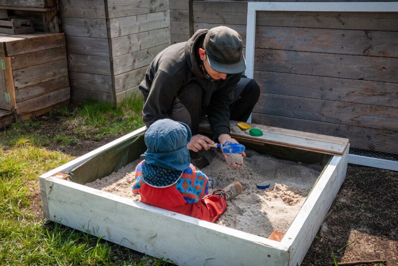 Sandkasten selber bauen: ein Mann und ein Kind spielen im Sand.
