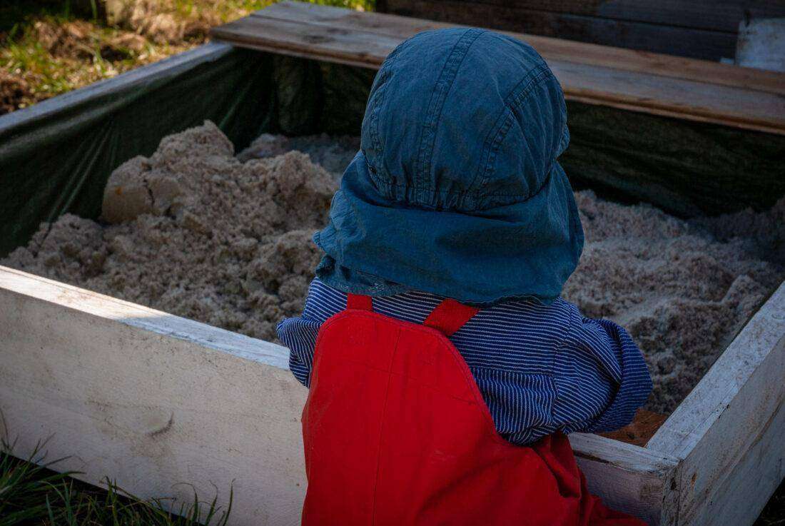 Ein Kind sitzt vor einem selbst gebauten Sandkasten. 