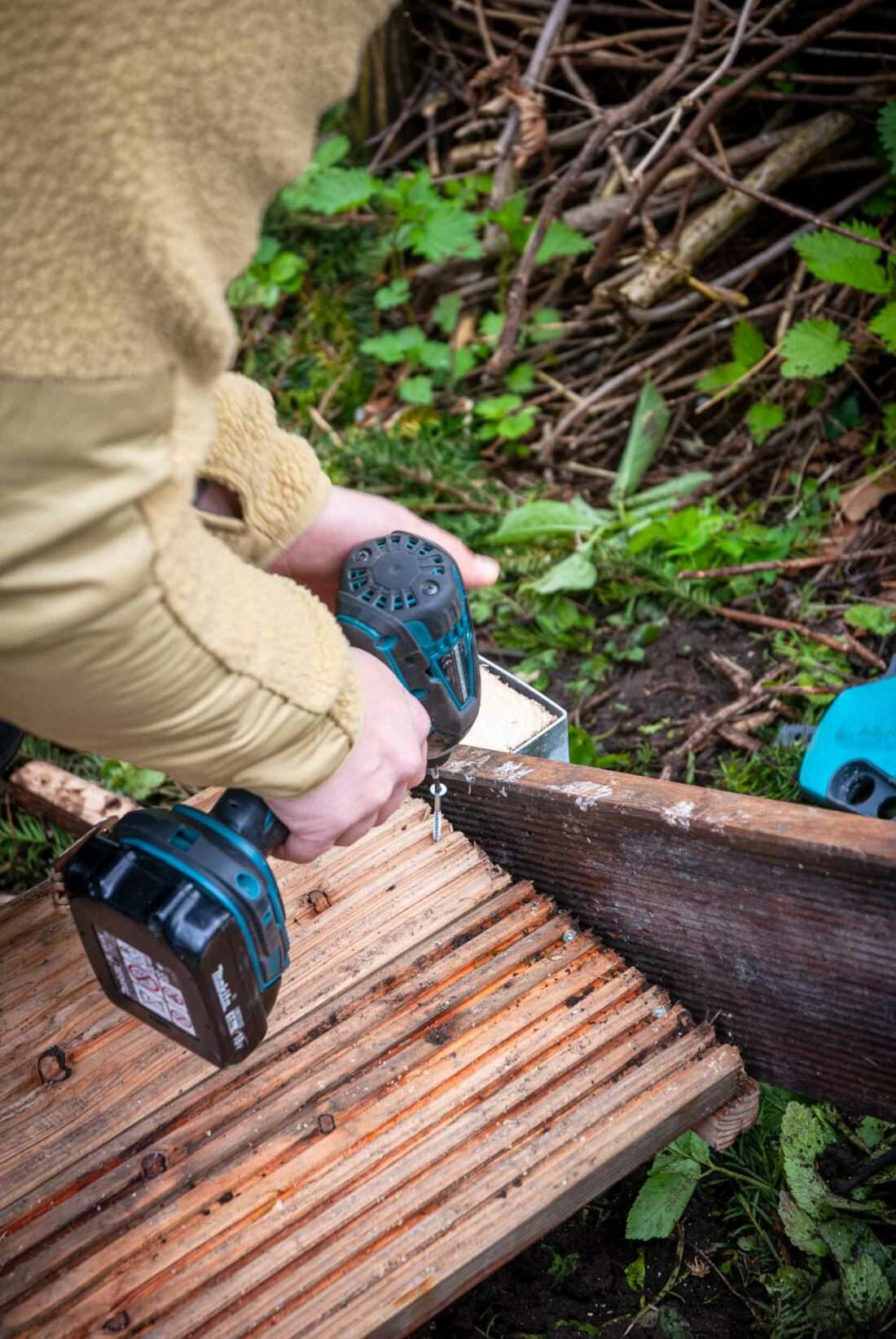 Eine Frau schraubt ein Brett an eine Wange einer selbst gebauten Holztreppe