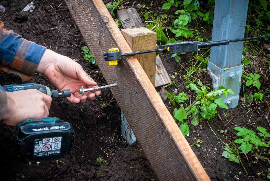 Ein Mann schraubt eine Wange einer selbst gebauten Holztreppe an einem Kantholz fest.