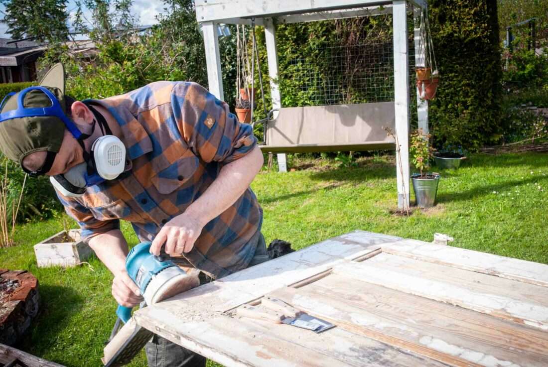 Ein Mann schleift die Kanten einer Tür ab, aus der ein Klapptisch gebaut wird.