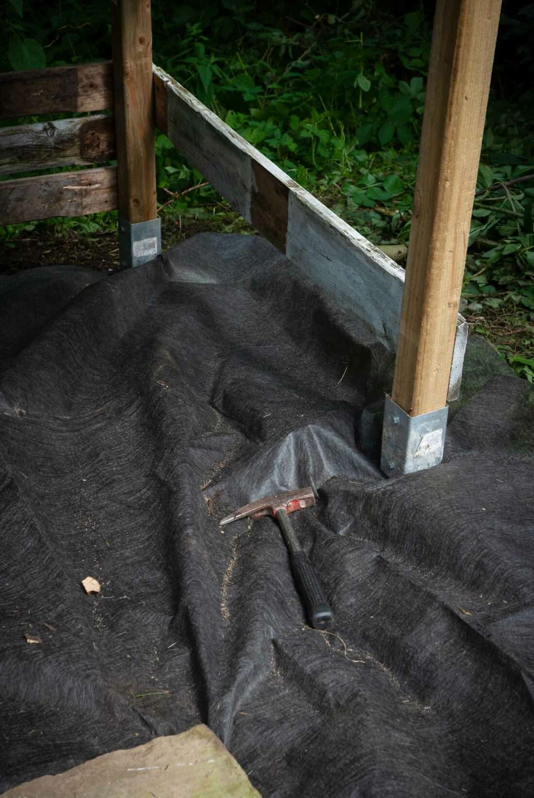 Unkrautvlies wird um die Unterkonstruktion eines selbst gebauten Spielhauses gelegt.