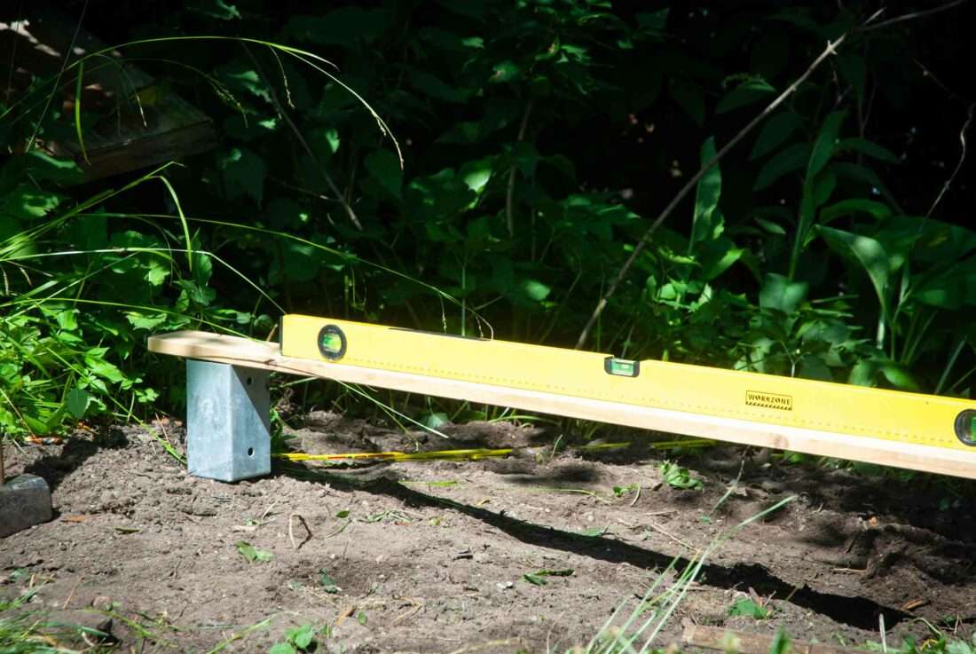Eine Wasserwaage liegt auf einem Brett, das auf einer Einschlagbodenhülse aufliegt.