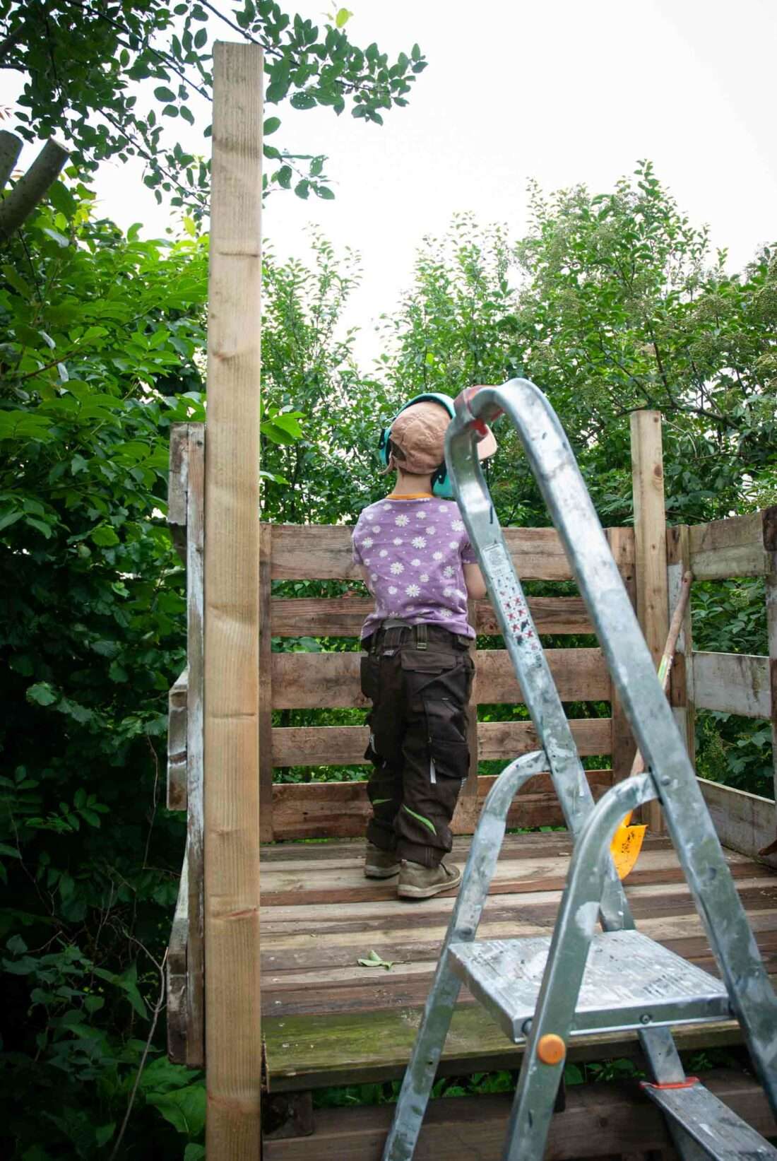 Spielhaus selber bauen: Ein Junge schraubt Bretter als Verkleidung einer Plattform an.