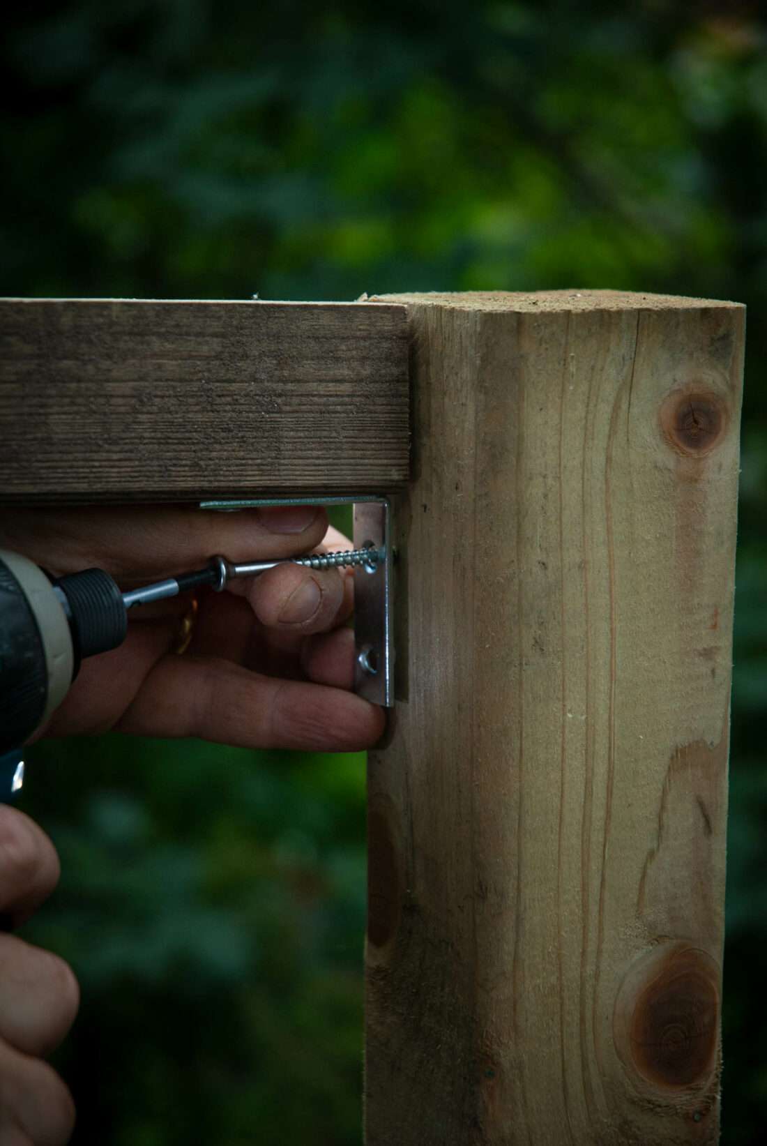 Detailansicht eines Akku-Schraubers, der eine Schraube durch einen Winkelverbinder treibt und zwei Hölzer miteinander verschraubt.