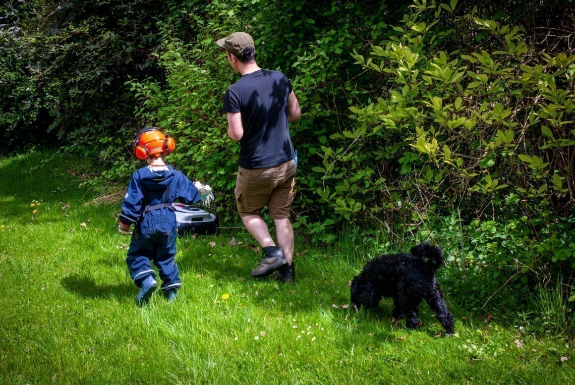 Ein Mann geht mit Kind und Hund durch einen Garten und steuert dabei einen ECOVAS Mähroboter
