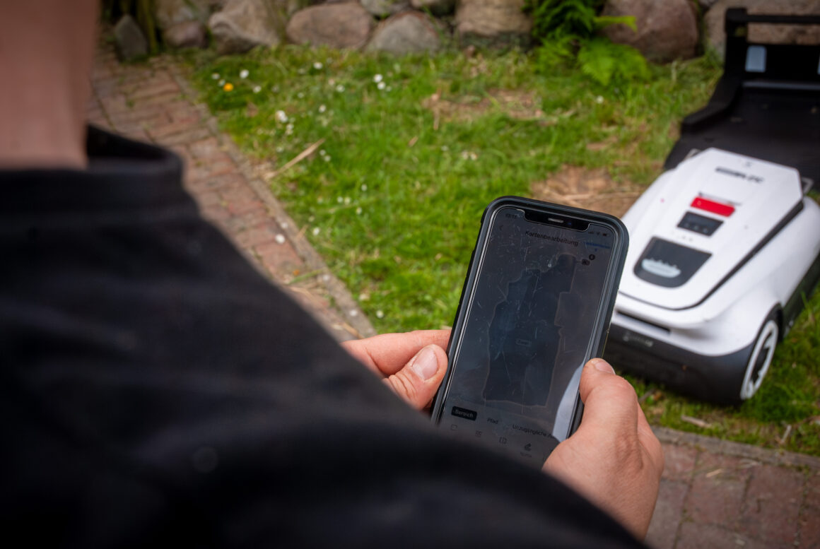 Ein Mann legt per App die Zonen für einen ECOVAS Mähroboter fest. 