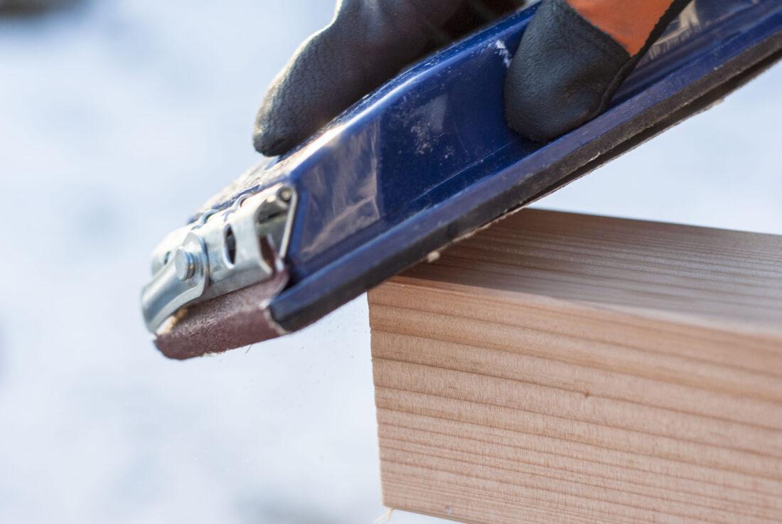 Mit einem Handschleifgerät wird ein Brett für ein DIY-Hochbeet geschliffen. 