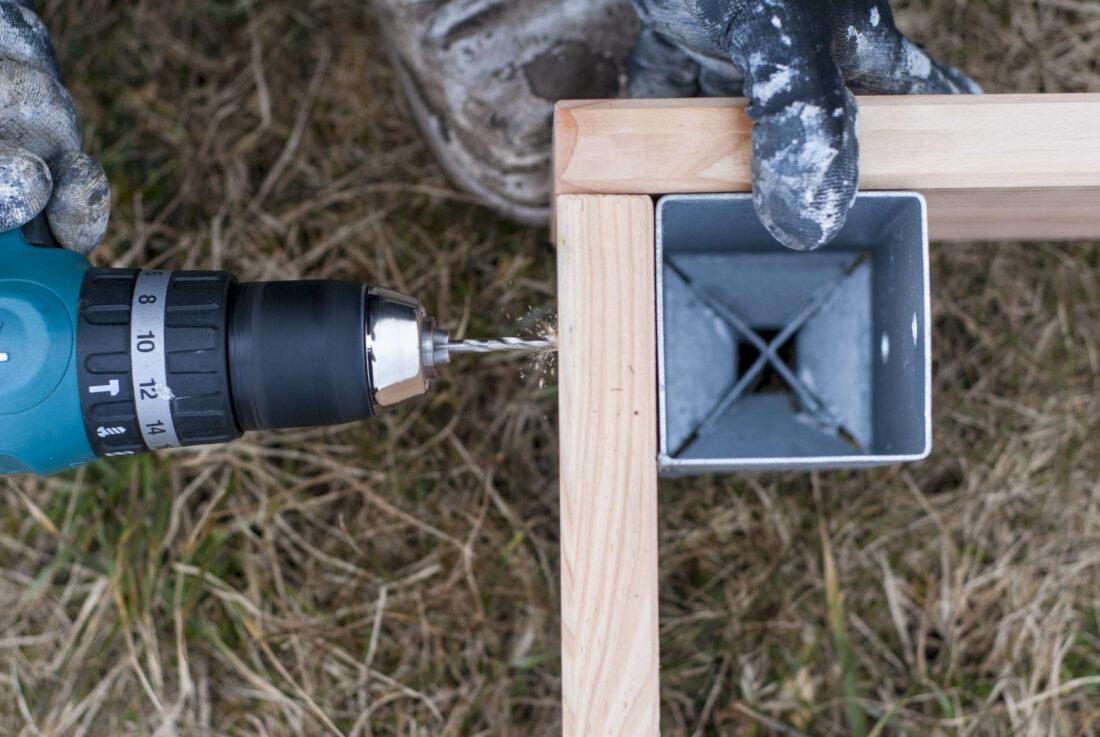 Vogelperspektive eines Hochbeet-Baus: Der Rahmen eines Hochbeets wird durch die Einschlaghülse am Kantholz festgeschraubt. 