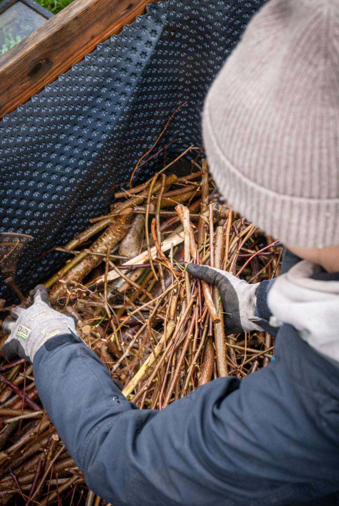 Eine Frau befüllt ein Hochbeet mit Zweigen. 