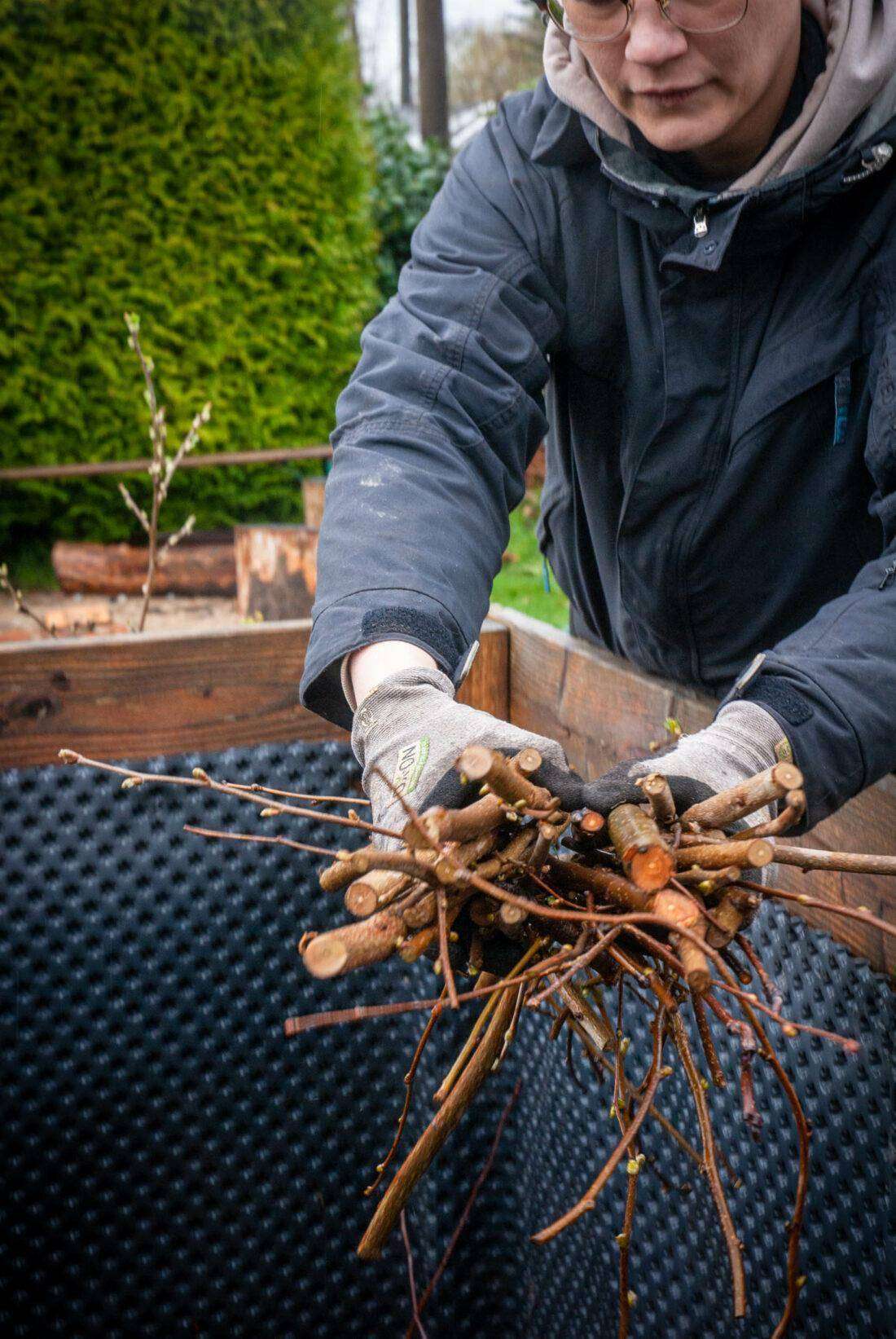 Eine Frau befüllt ein Hochbeet mit Ästen. 