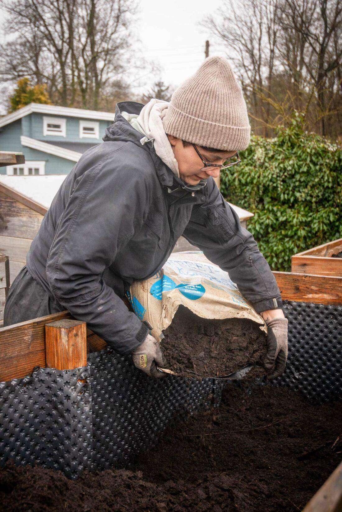 Eine Frau leert einen Sack Hochbeet-Kompost in ein Hochbeet. 