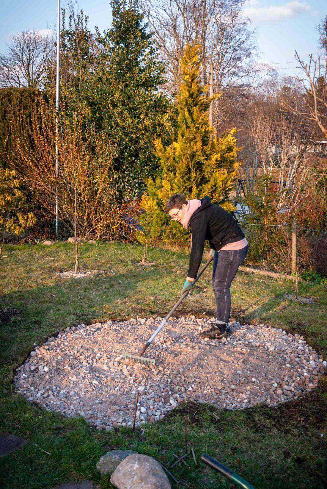 Eine Frau bringt eine erste Drainageschicht für eine Kräuterspirale auf. 