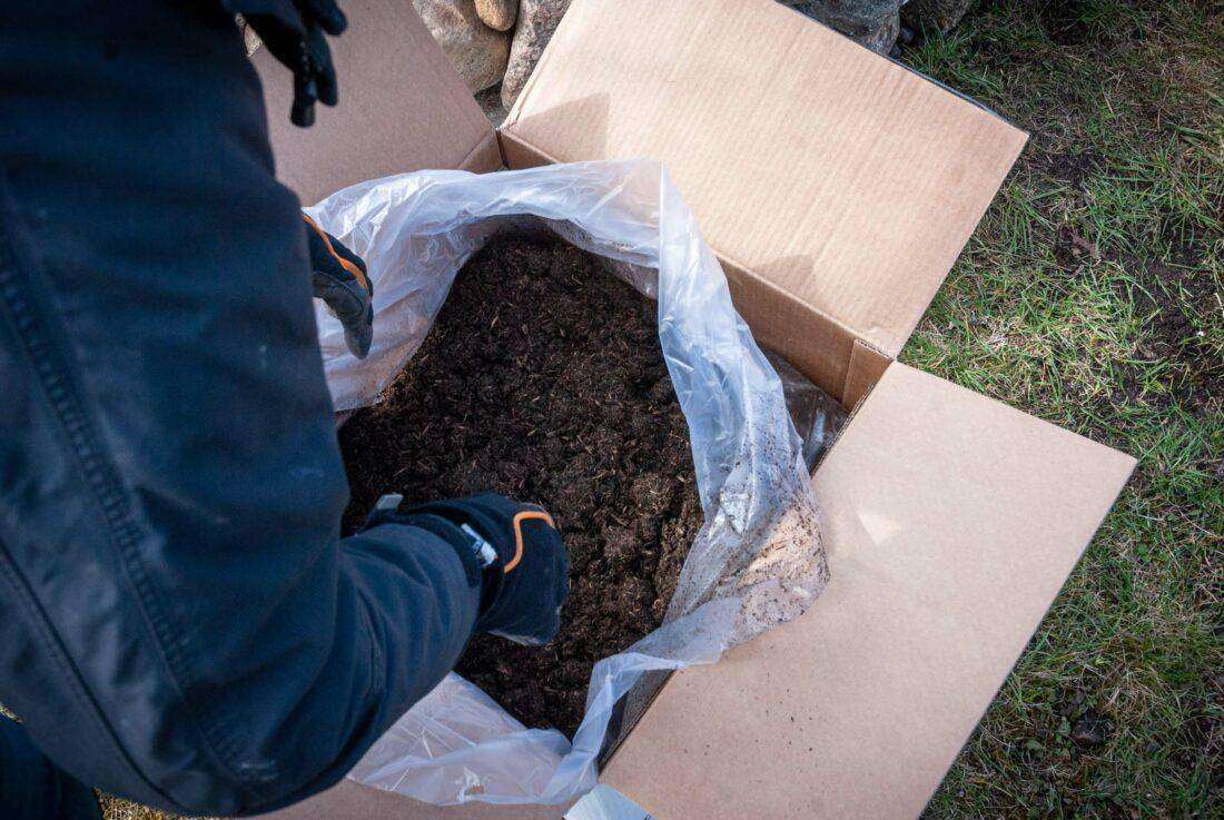 Kräuterspirale mit Erde befüllen:Over-the-shoulder-Schuss in einen Karton der Firma Floragard. 