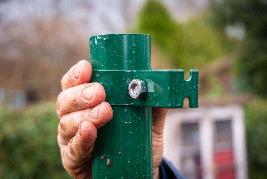 Ein mann befestigt Bügel an einem Zaunpfosten für deinen Sichtschutz an einer Terrasse. 