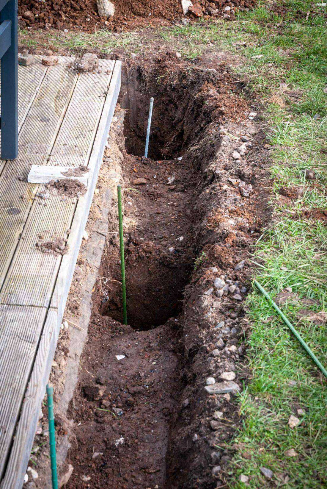 Neben einer Holzterrasse sind Löcher für die Pfosten eines Sichtschutzes gegraben. 