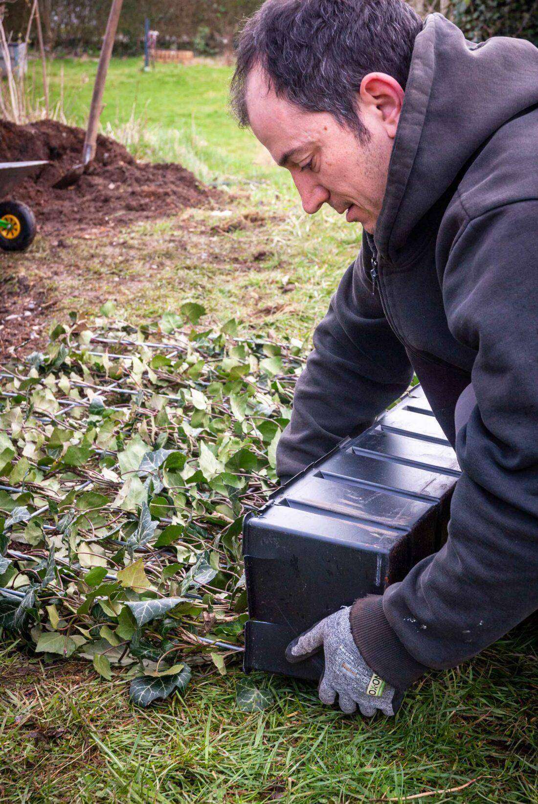 Sichtschutz Terrasse: Ein Mann bereitet das Einpflanzen eines Zaunelements vor. 