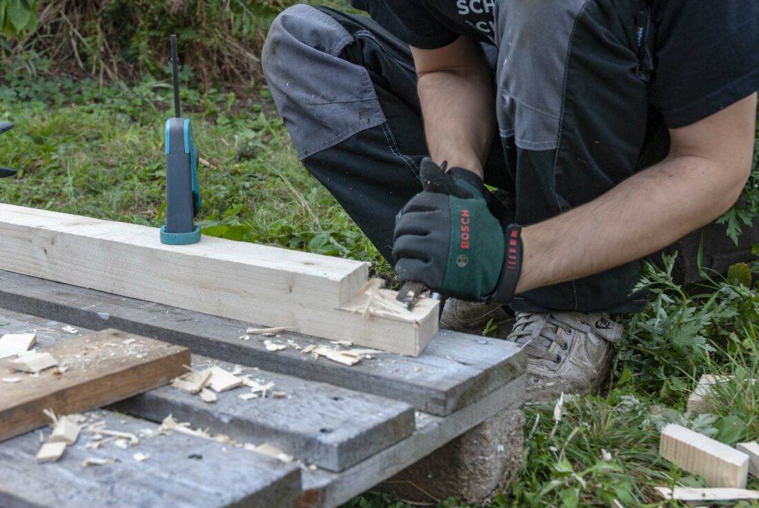 Gewächshaus selbst bauen: Ein Mann stemmt ein Stück aus einem Kantholz. 