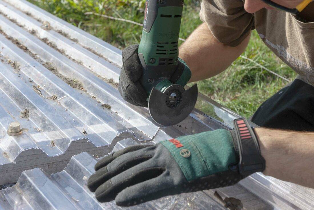 Gewächshaus selbst bauen: Ein Mann sägt mit einem Multitool eine Plexiglasplatte zurecht. 