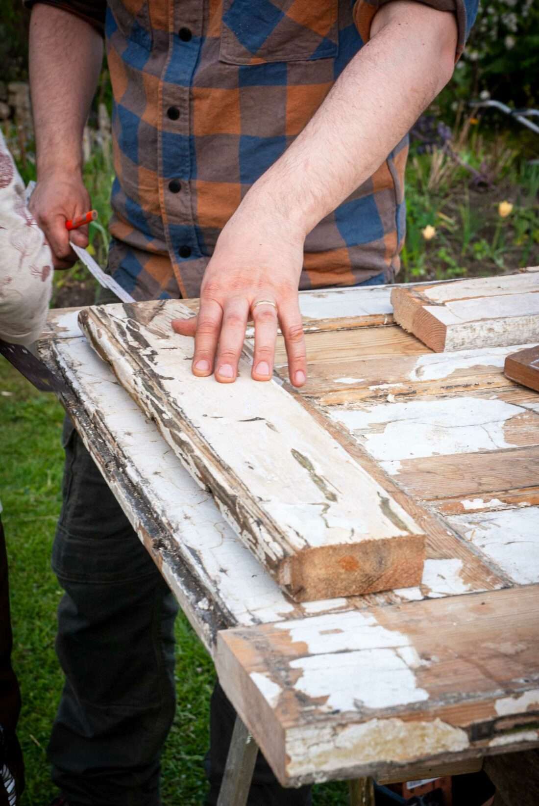 Ein Mann misst ein Stück Holz zu, an dem Tischbeine für einen Klapptisch montiert werden.