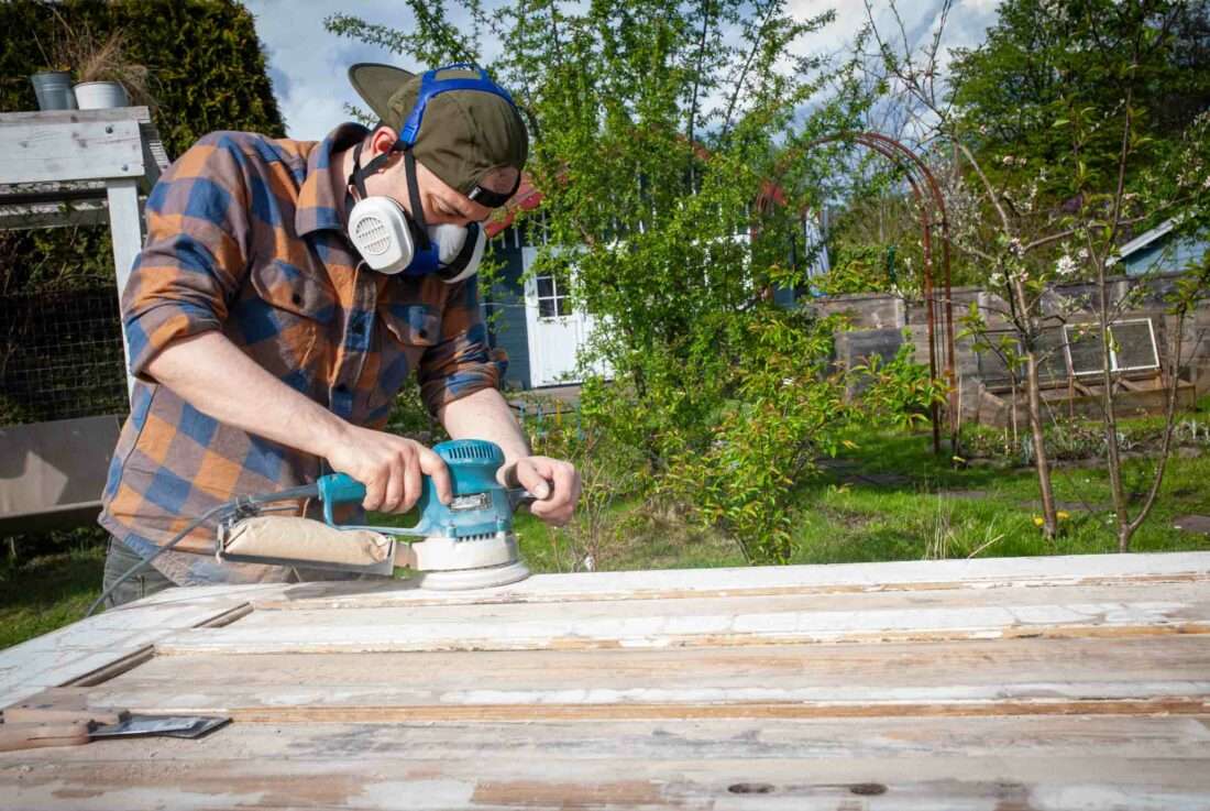 Ein Mann schleift eine alte Tür ab, aus der ein Klapptisch gebaut werden soll.
